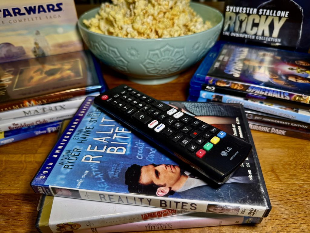stack of dads with remote on top and bowl of popcorn in the background